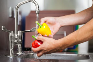 Kitchen porter washing pepper under running tap